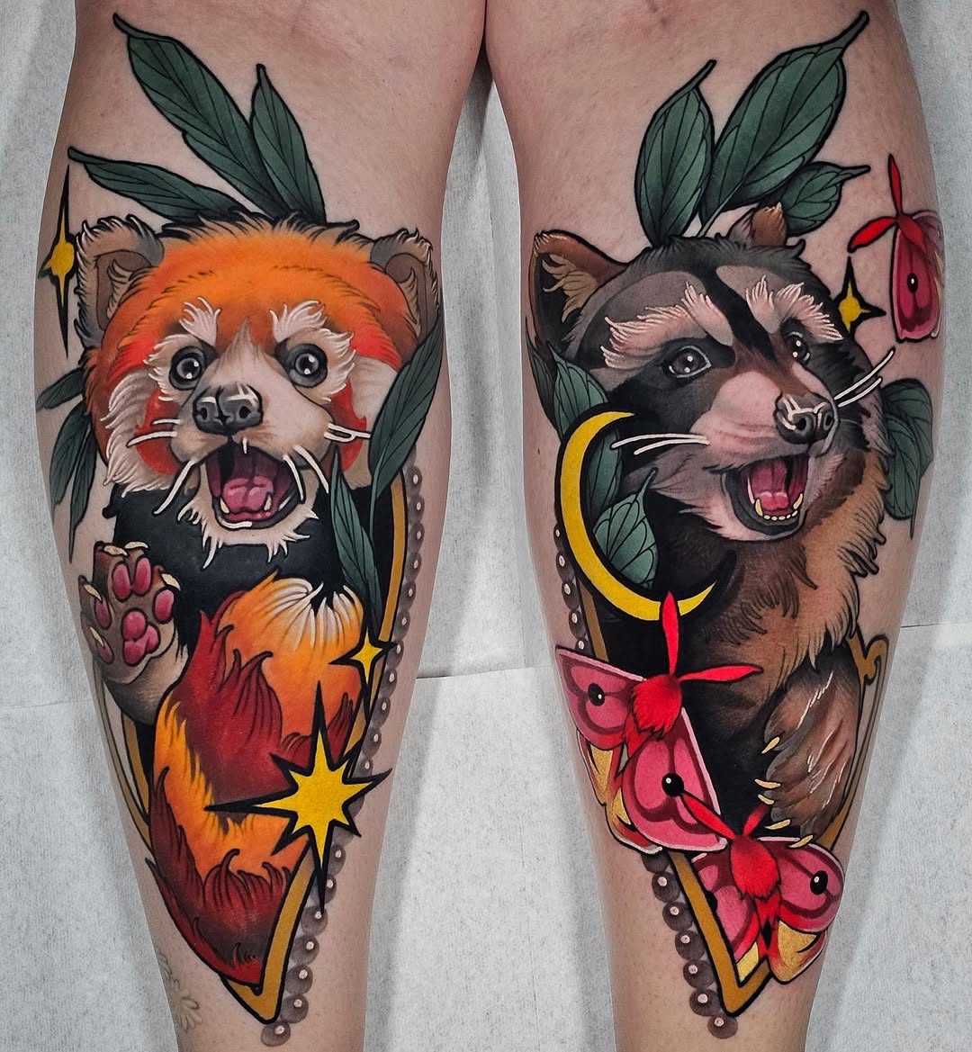 Two matching leg tattoos featuring anthropomorphic raccoons with open mouths surrounded by botanical elements, flames, moons, and stars in orange, red, yellow, and green.