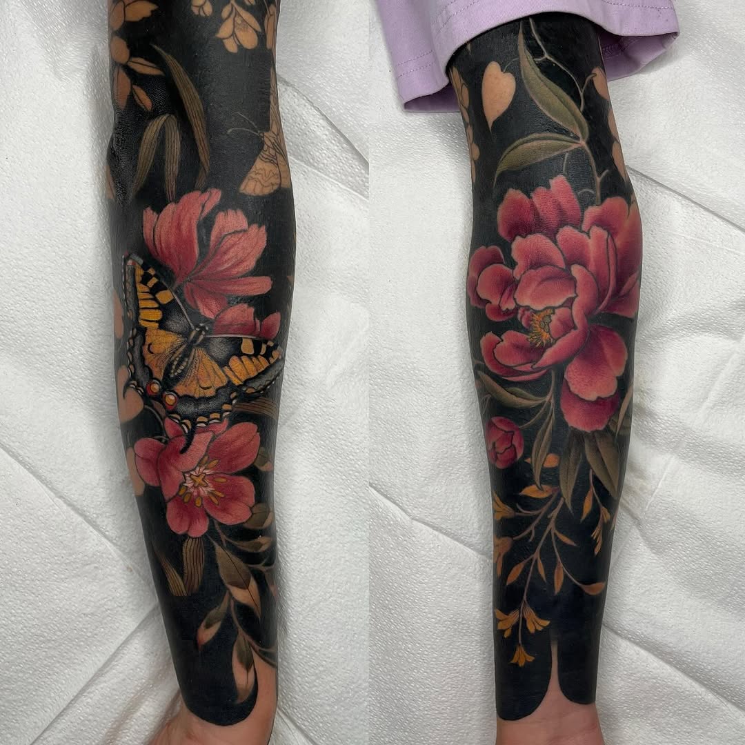 Matching sleeve tattoos featuring red peonies, golden butterflies, and bronze foliage on a dark background covering both forearms.