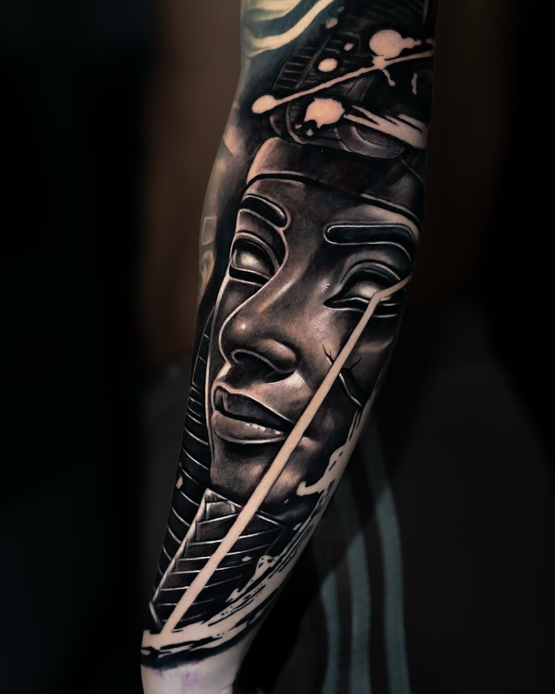 Detailed portrait tattoo on forearm featuring a face with dramatic shading, fine line details, and geometric elements in black and grey ink.
