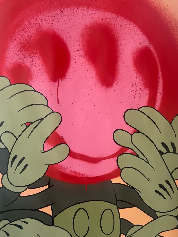 Cartoon hands with white gloves and black outlines holding a large pink smiling face with two dark eyes against a red and orange background.