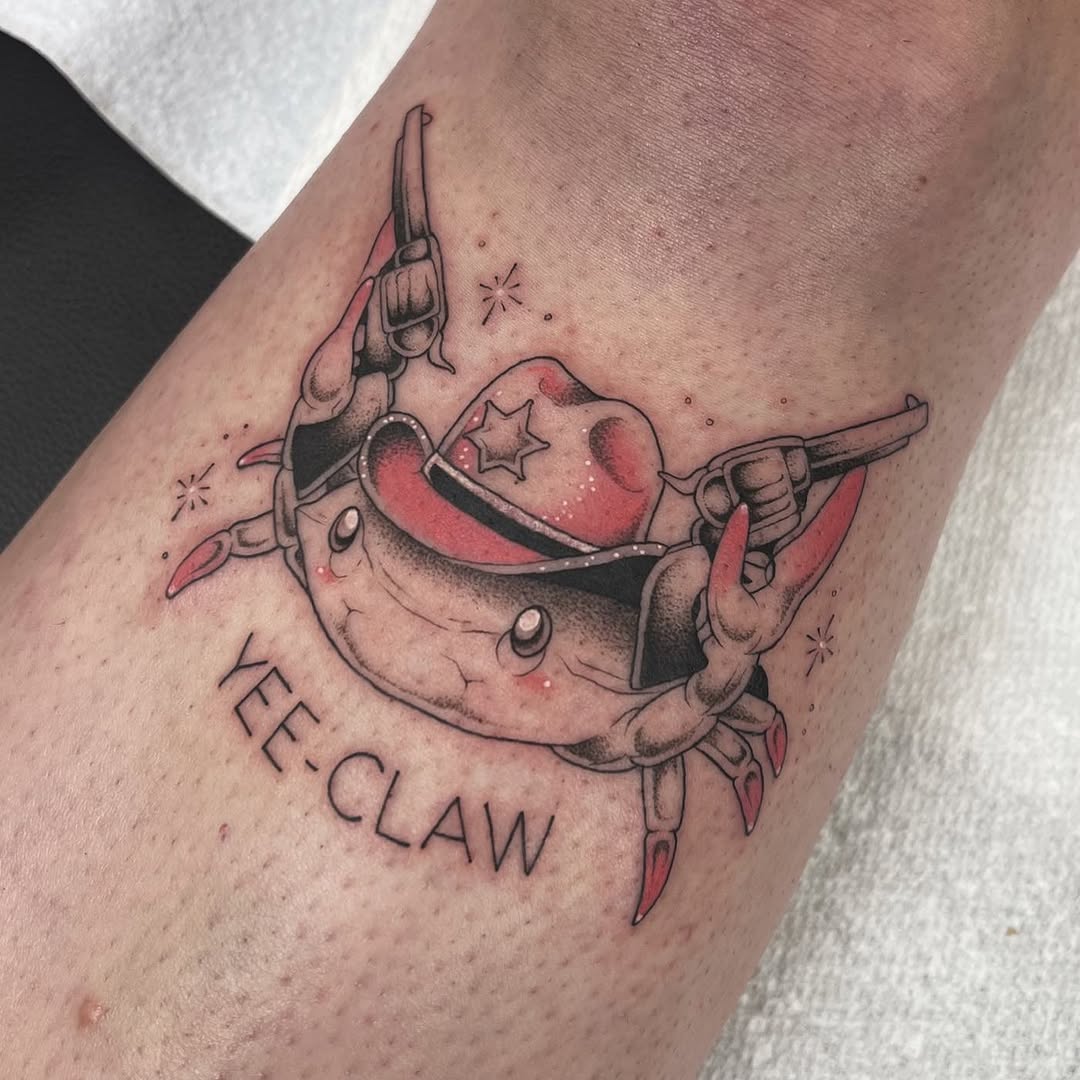Colorful tattoo of a smiling crab wielding two revolvers with a cowboy hat, surrounded by stars and the text "YEE CLAW" on an arm.