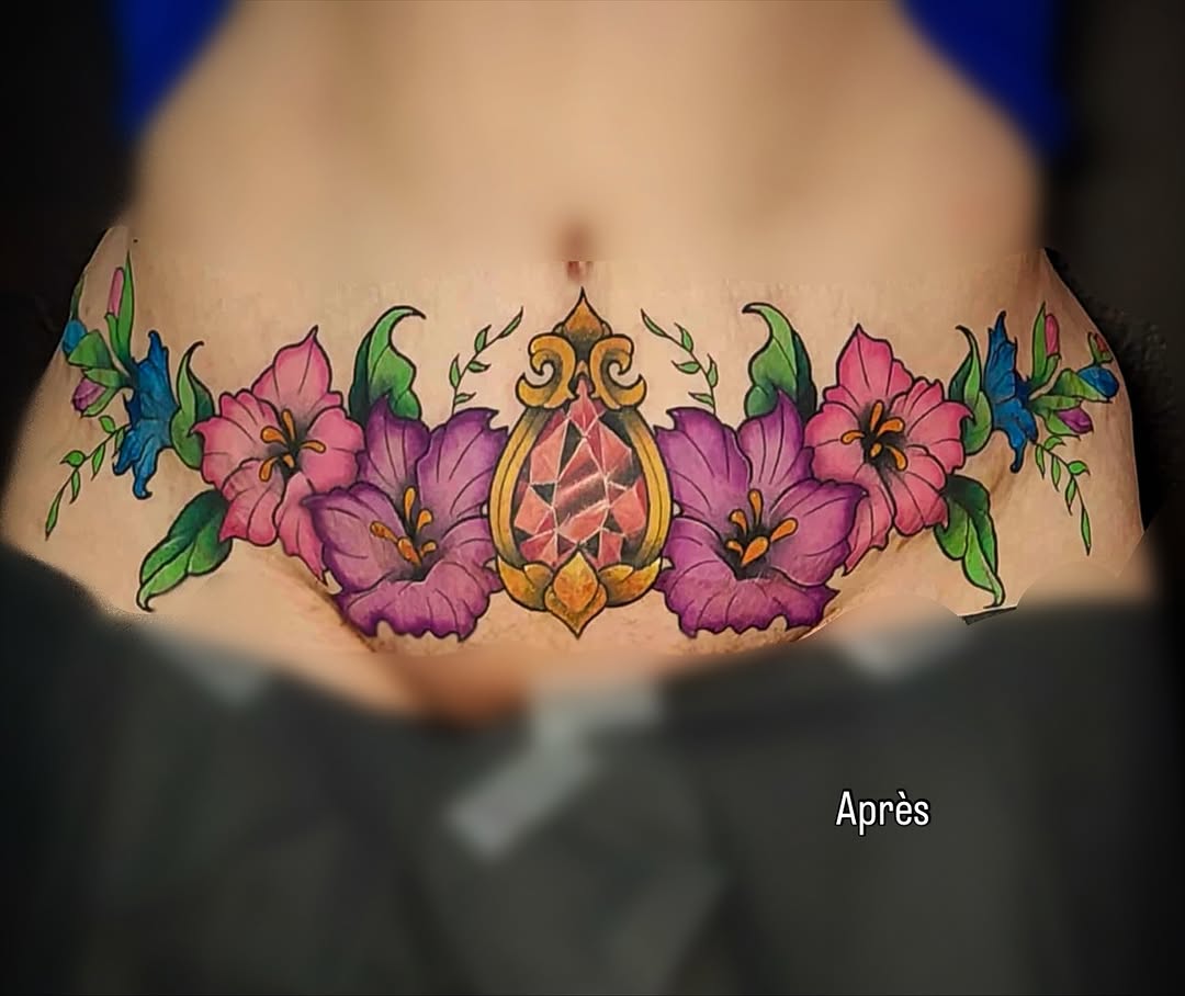 Colorful sternum tattoo featuring pink and purple flowers with blue accents, a golden ornamental pendant, and green foliage arranged symmetrically around the chest.