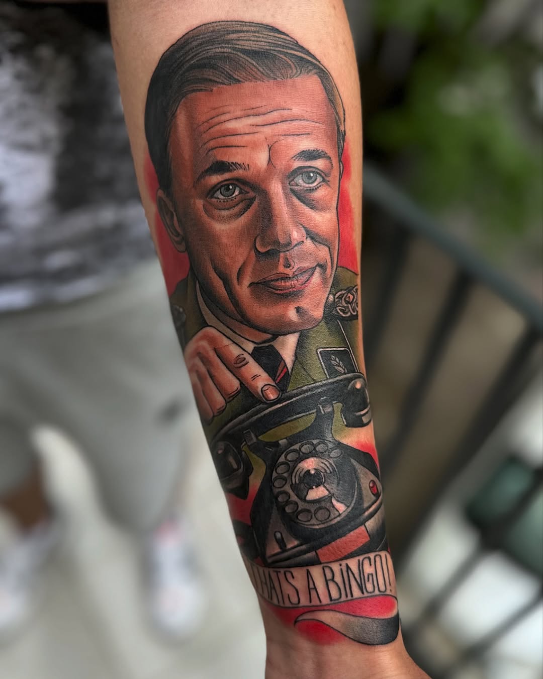 Colored arm tattoo featuring a man's portrait in red and flesh tones holding a rotary telephone, with text reading "THAT'S A BINGO" below.