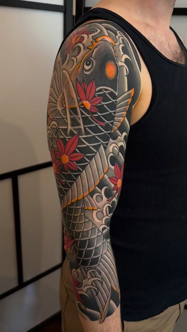Full-sleeve arm tattoo featuring a koi fish with red flowers, intricate scales, ornamental patterns in black, gray, orange, and red.