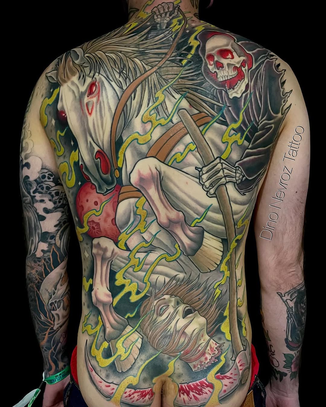Back piece tattoo featuring a skeletal grim reaper with horse, bones, and flowing robes in red, yellow, green, and grey colors.