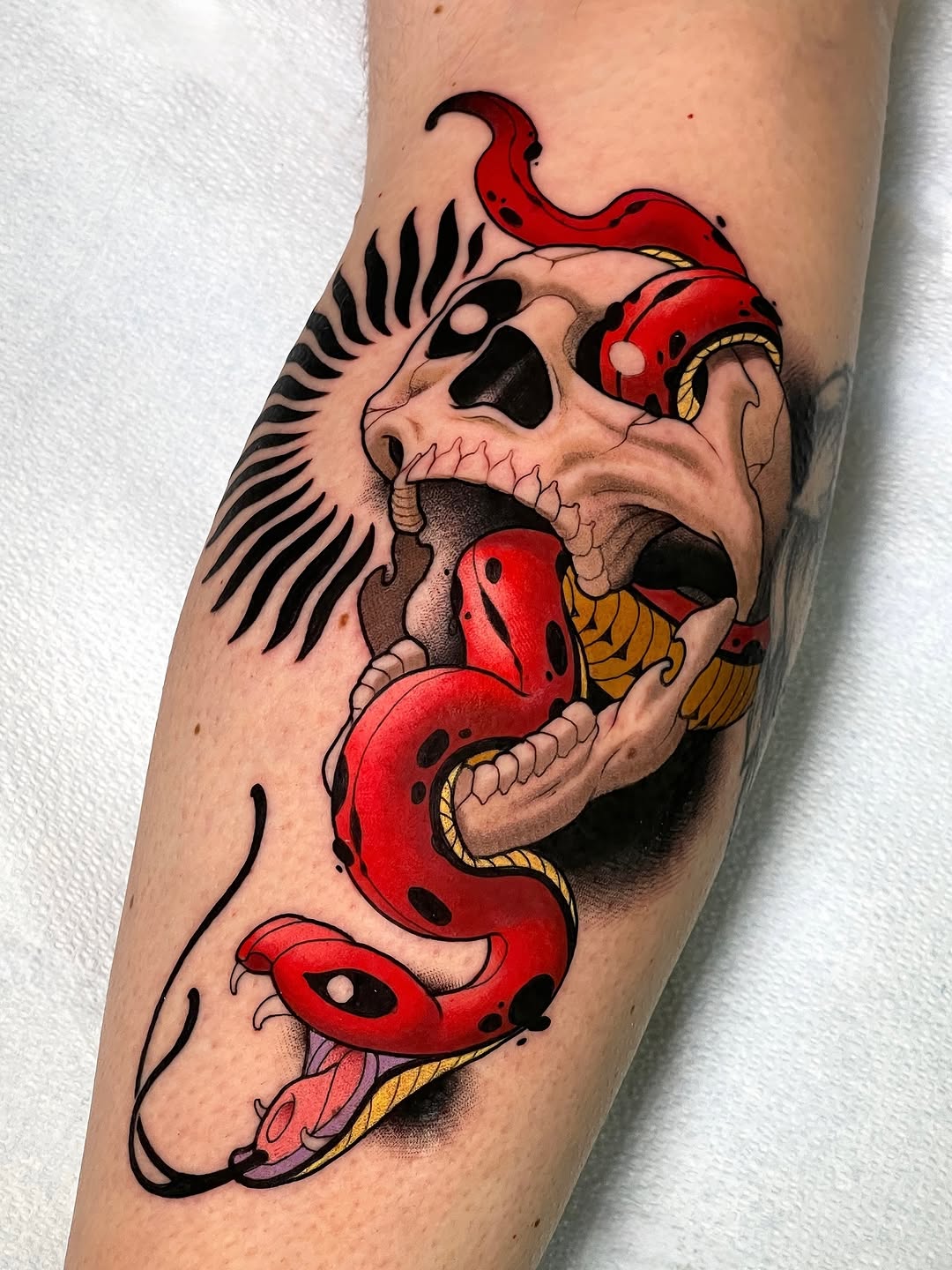 Skull with wings and red serpent wrapping around it, featuring gold accents, tattooed on the upper arm.