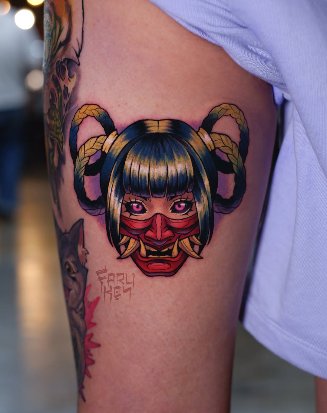 Colorful tattoo on upper arm featuring an anime-inspired female character with twin buns, pink eyes, and red demon-like facial markings in gold, black, and red tones.