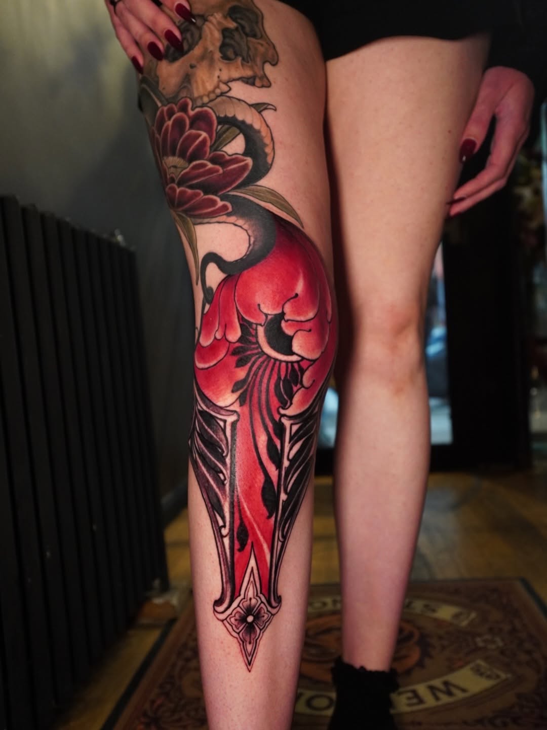 Full-leg tattoo featuring red flowers, black botanical details, and ornamental elements extending from thigh to ankle.