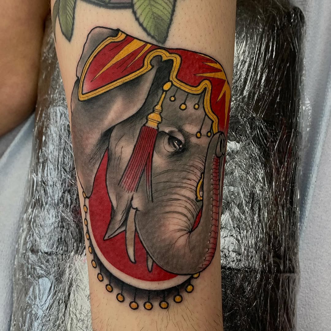 Elephant head wearing a red and gold ornate headdress with tassels and beaded details on an upper arm, featuring gray and red coloring.