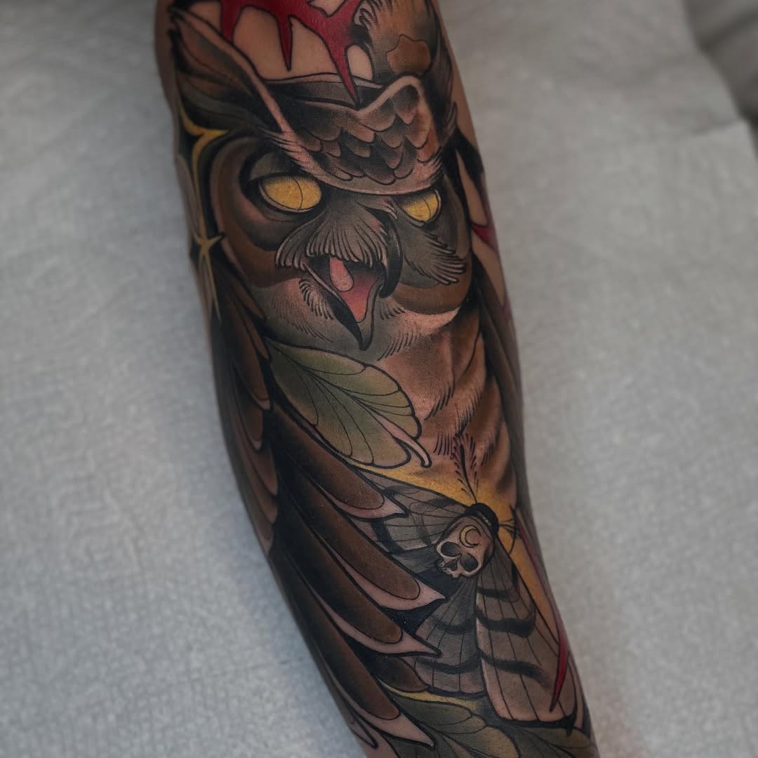 Owl tattoo on forearm featuring golden eyes, brown and red tones, with detailed feathers and wing elements wrapping around the arm.