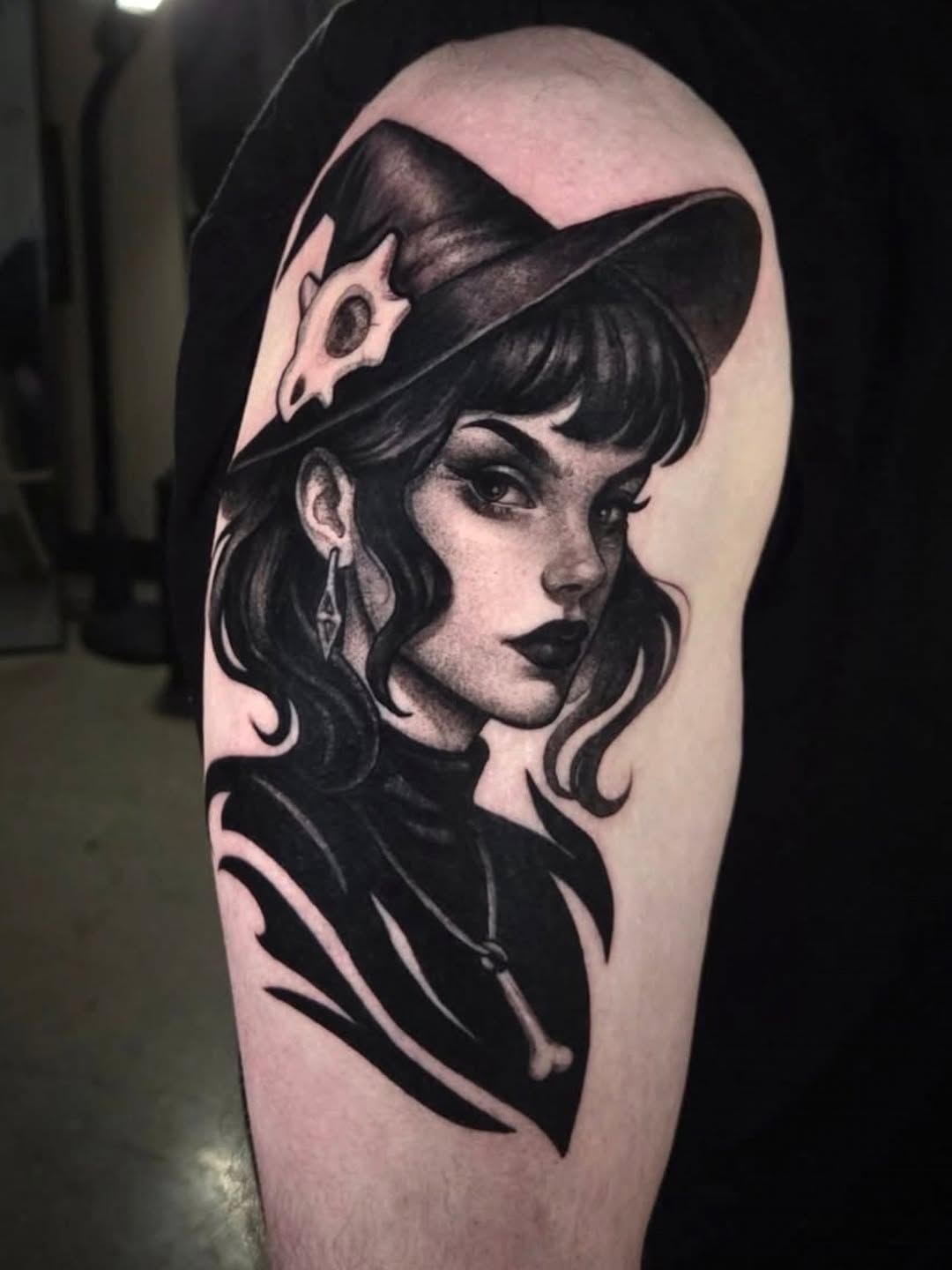 Black ink portrait tattoo of a woman with wavy dark hair and a feathered hat, featuring detailed shading on the upper arm.