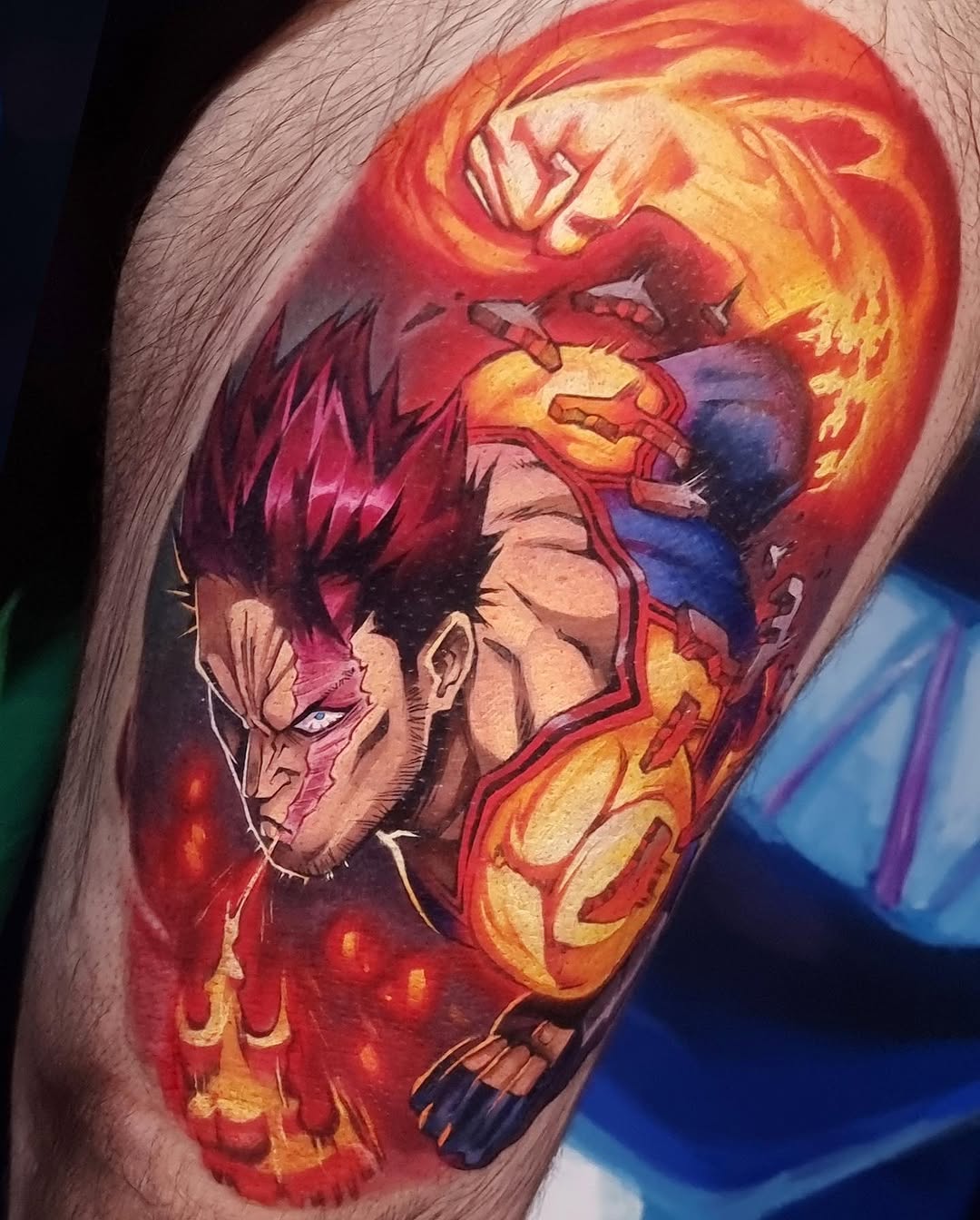Colorful upper arm tattoo featuring a character with spiky red hair and an angry expression, surrounded by flames in shades of orange, yellow, and red.