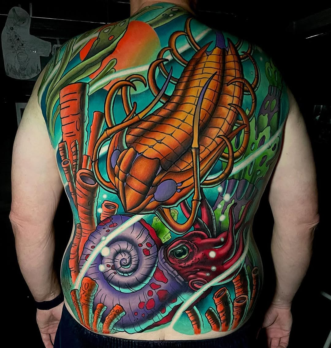 Colorful back tattoo featuring a large orange crustacean, purple spiral shell, red creature, and green foliage against a turquoise background.