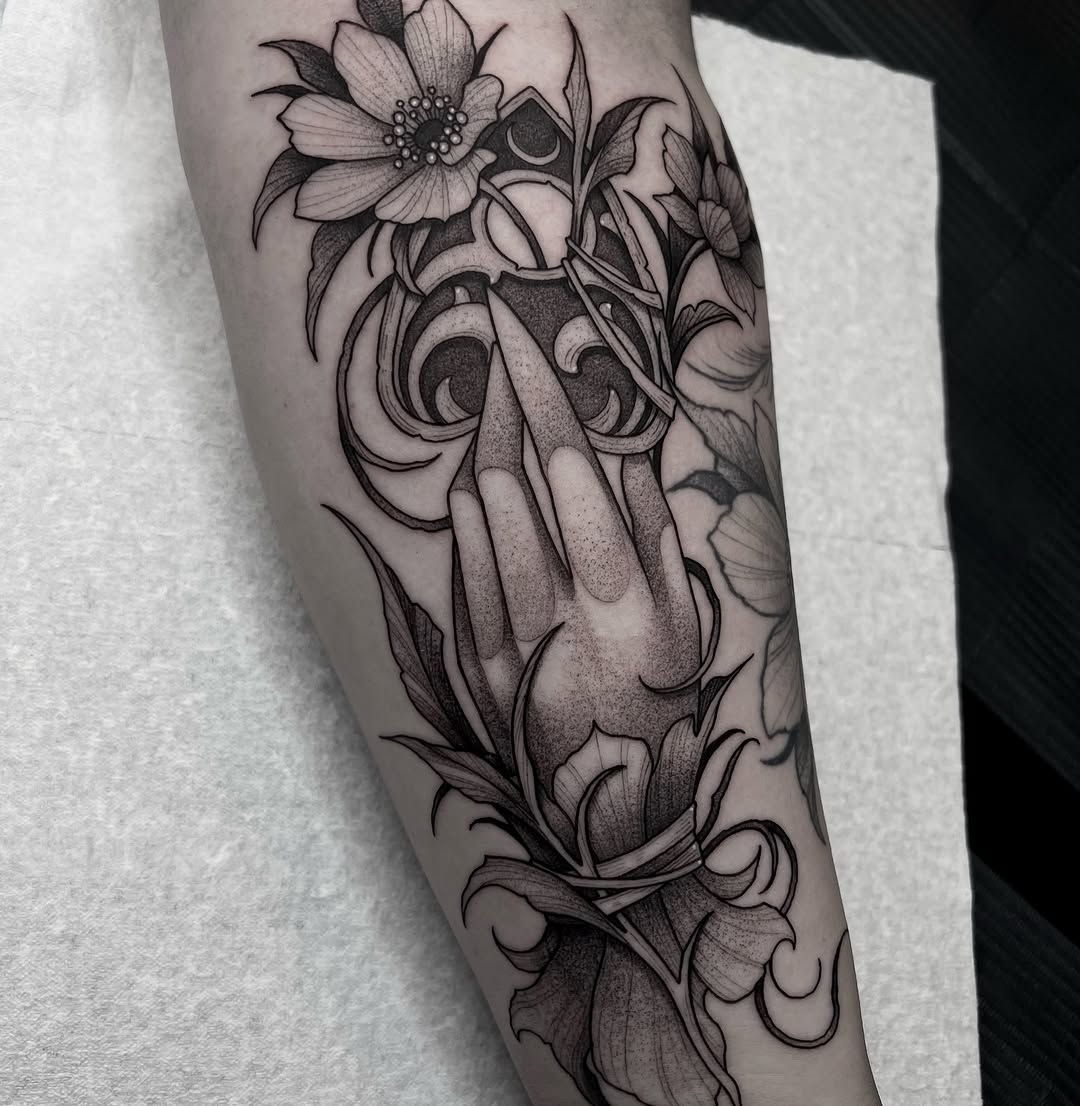 Hand holding ornamental flowers and scrollwork with moon phases, rendered in black ink on forearm.
