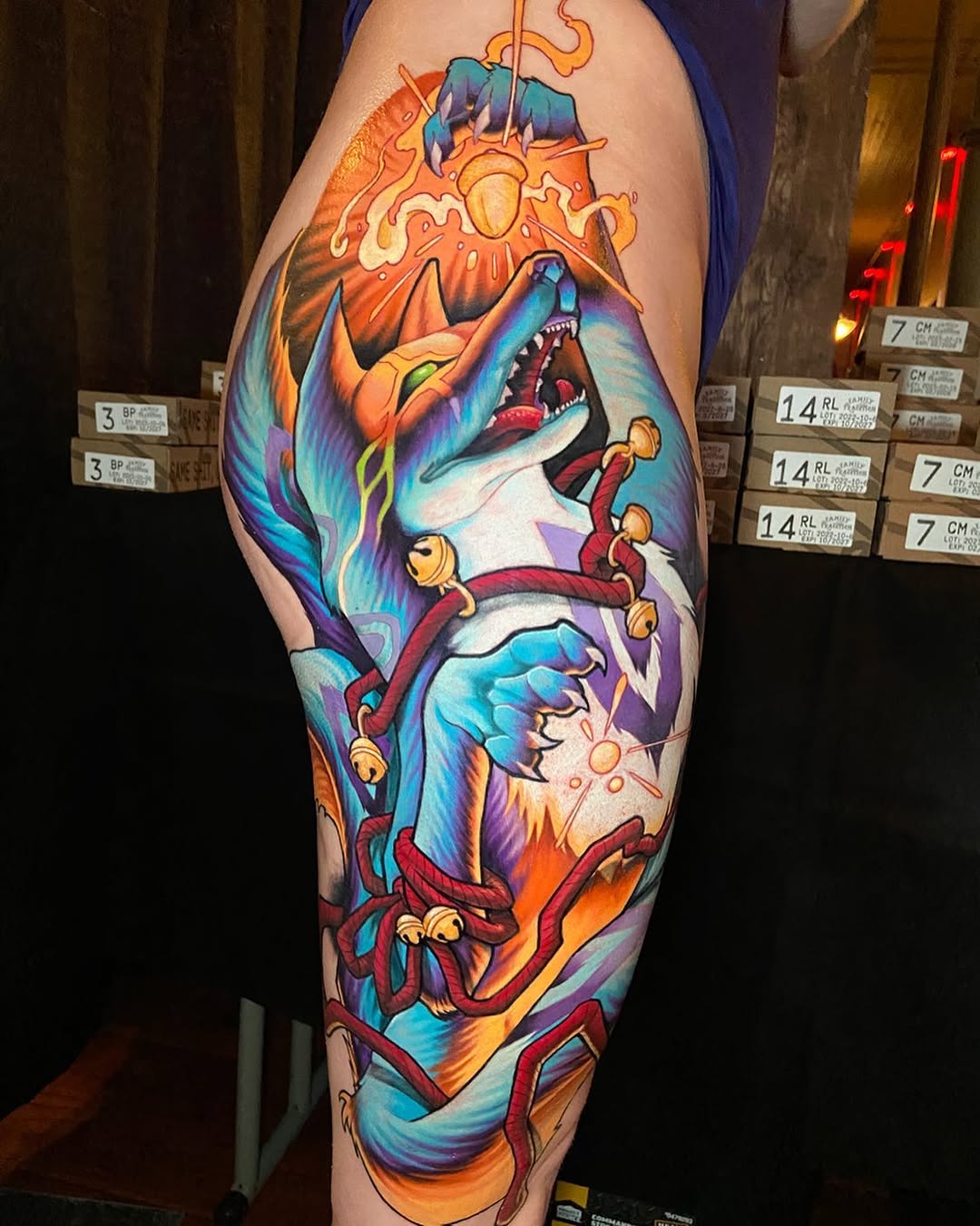 Colorful leg tattoo featuring mythological creatures and figures with orange, blue, and red hues, displayed on the thigh and calf area.