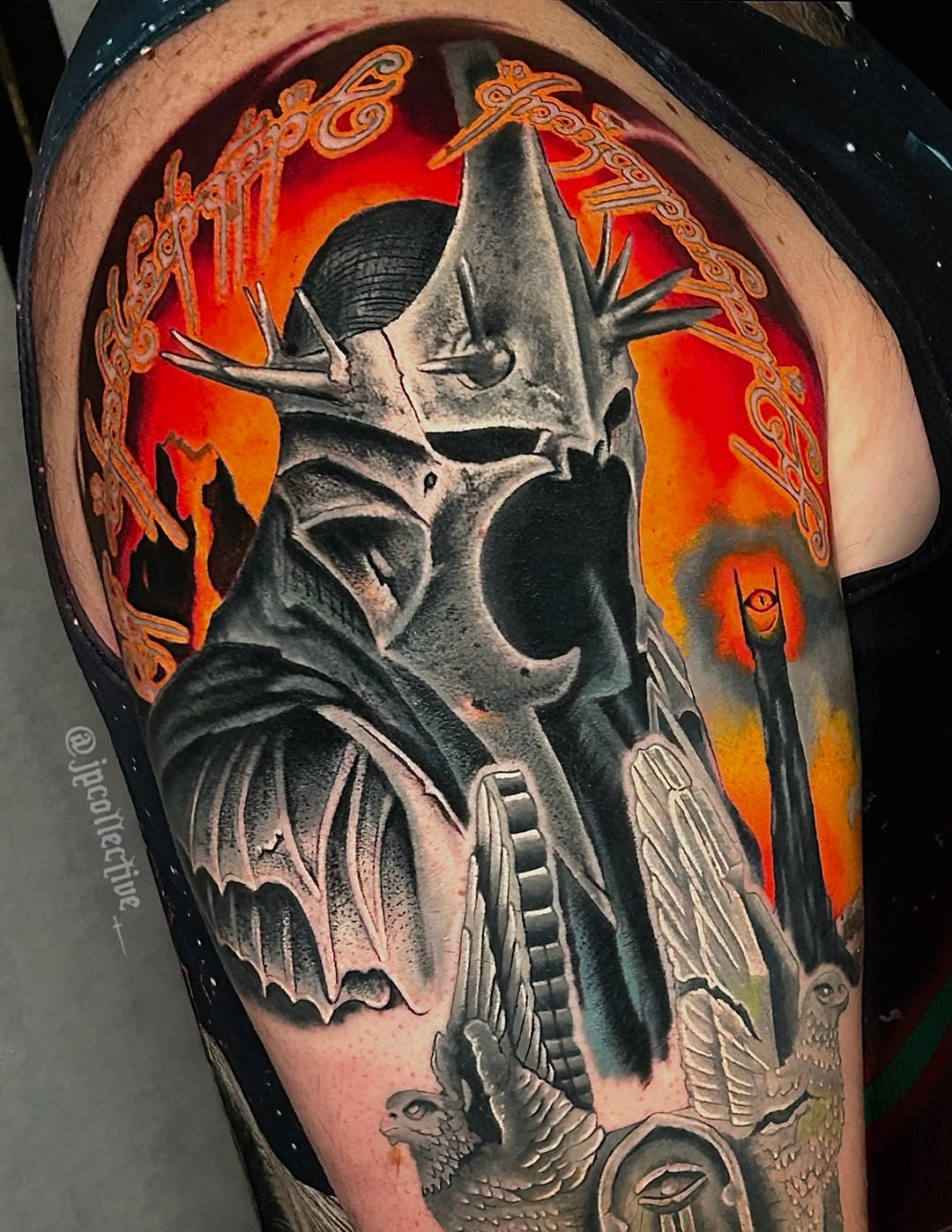 Elaborate shoulder tattoo featuring a horned skull with ornate gold decorative borders and a fiery red-orange background with additional mystical elements.