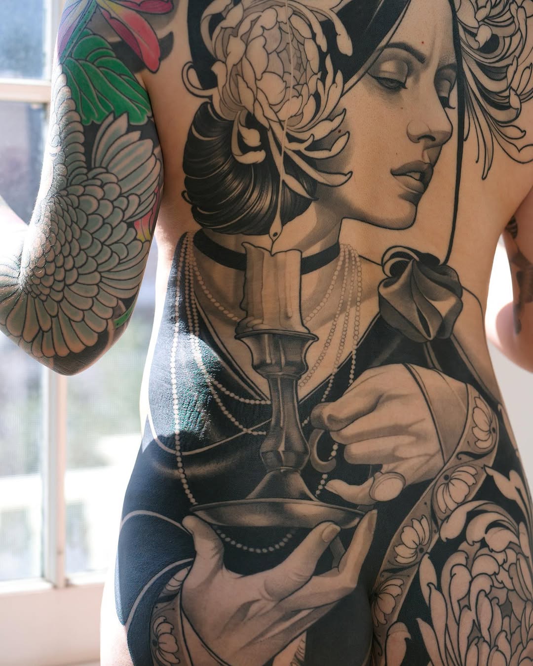 Portrait of a woman with ornate hair holding a chalice, accompanied by winged figures on the arms, rendered in black ink and green color accents on the torso and sleeves.