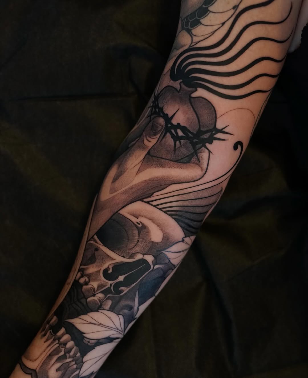Full-sleeve tattoo featuring an ant, wavy lines, floral elements, and additional insects in black and gray tones on an arm.
