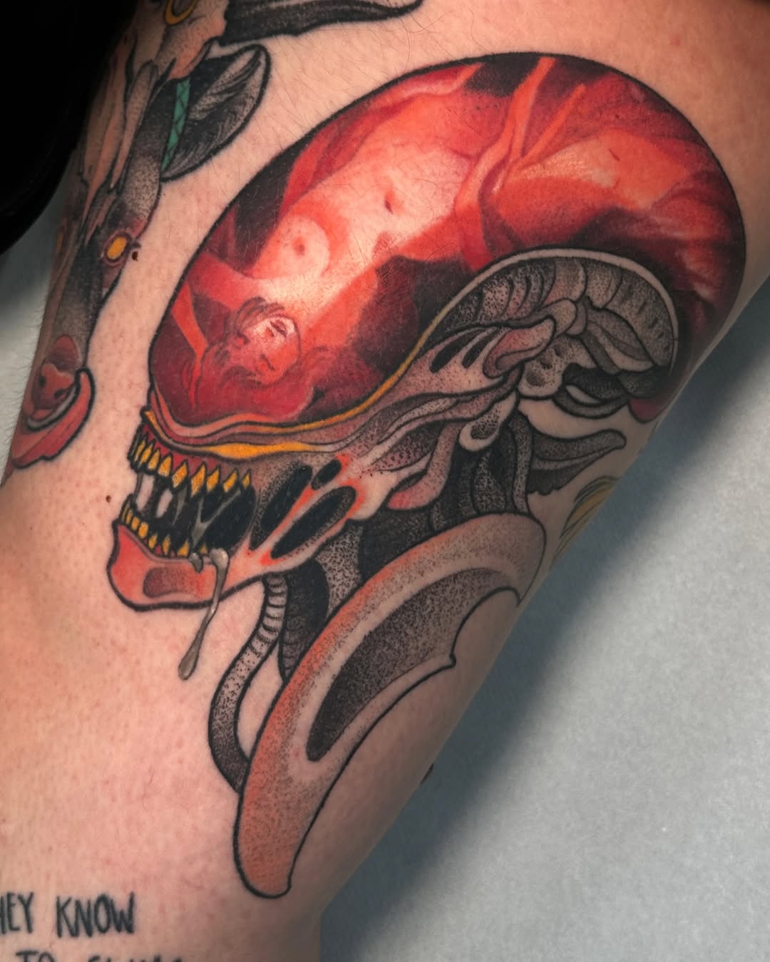 Anatomical skull tattoo with glowing red brain, golden teeth details, and black line work on upper arm, with partial text visible below.