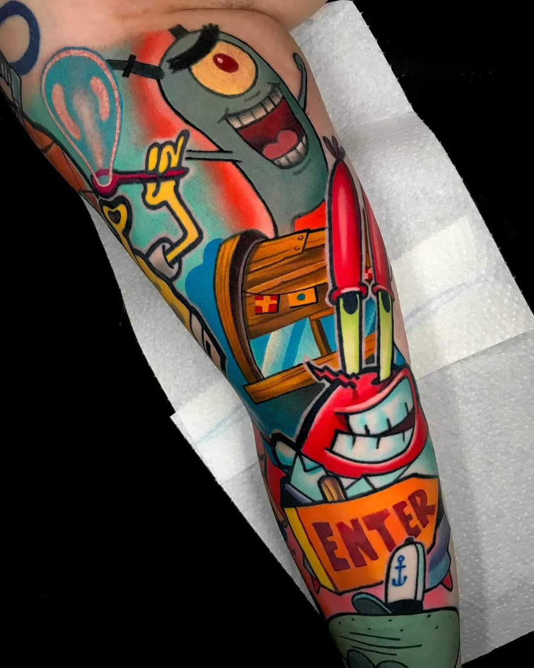 Colorful leg tattoo featuring a grinning zombie character holding a paddle, wooden chest, and anchor with "CENTER" text on the forearm.