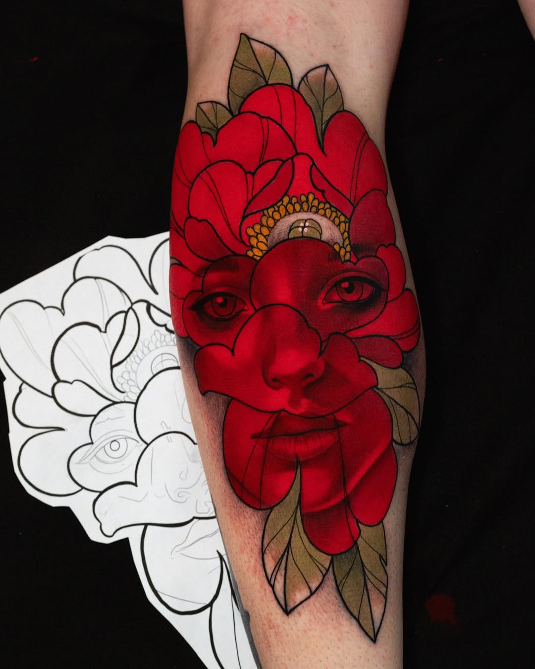 Completed red flower face tattoo on forearm with golden center and brown leaves, shown alongside sketch outline on white paper.