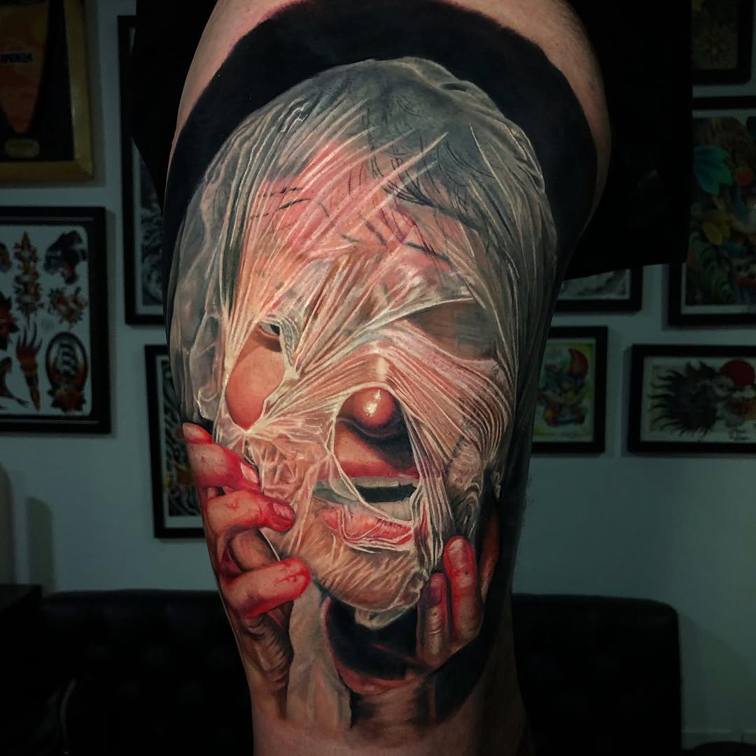 Colorful shoulder tattoo depicting a pale-skinned figure with long hair and glowing red eyes, rendered in red, gray, and flesh tones.