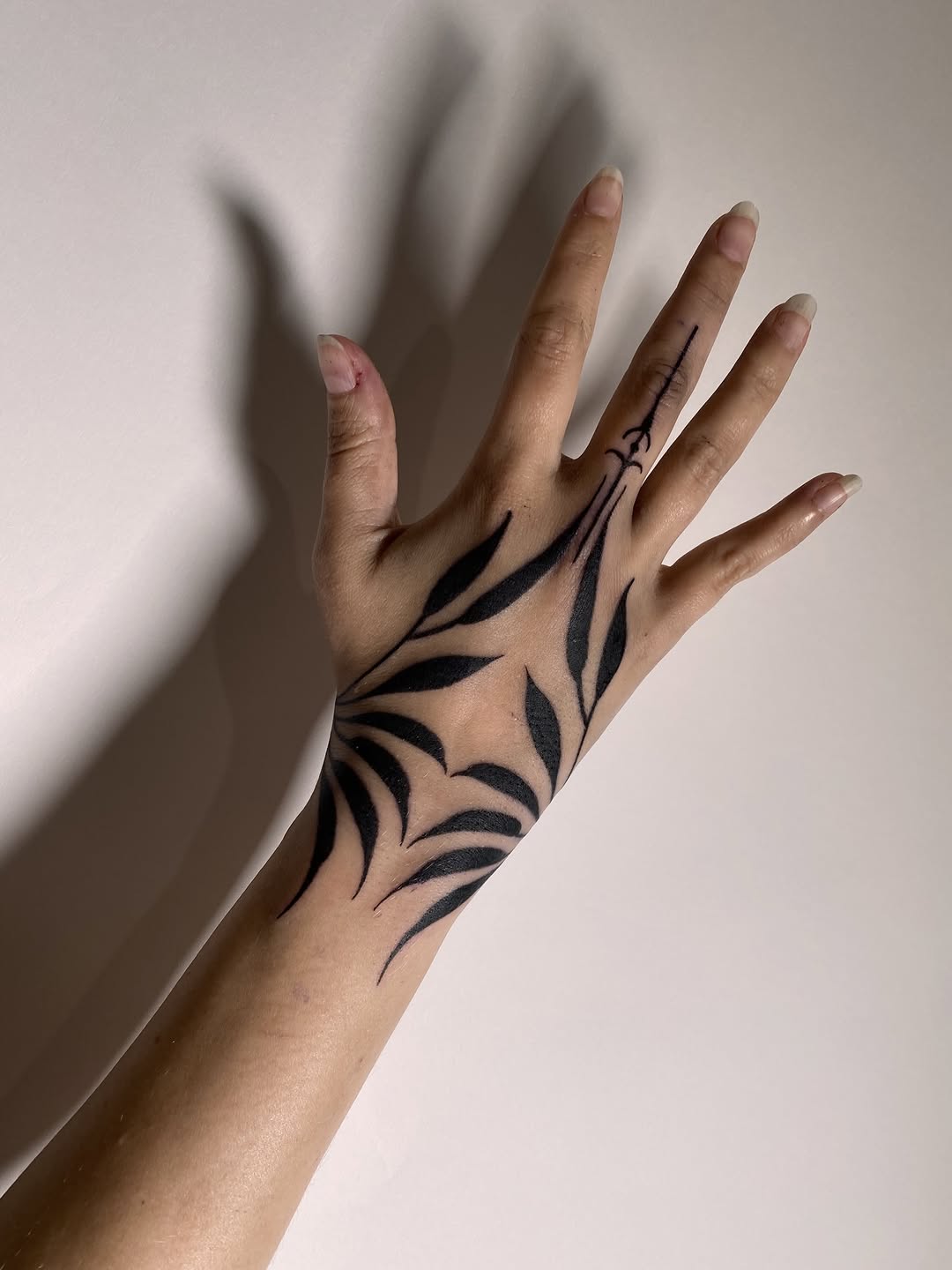Open palm displaying black curved leaf designs spanning from wrist to fingers against pale skin with natural lighting.