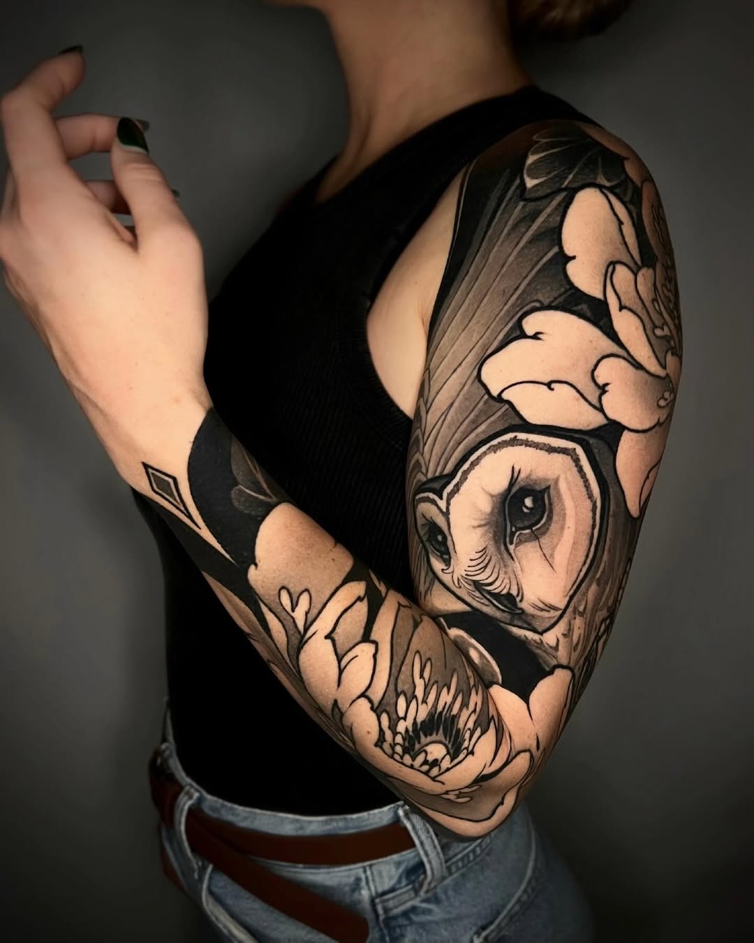 Full sleeve tattoo on right arm featuring an owl face, skull, clouds, and botanical elements in black and grey ink.