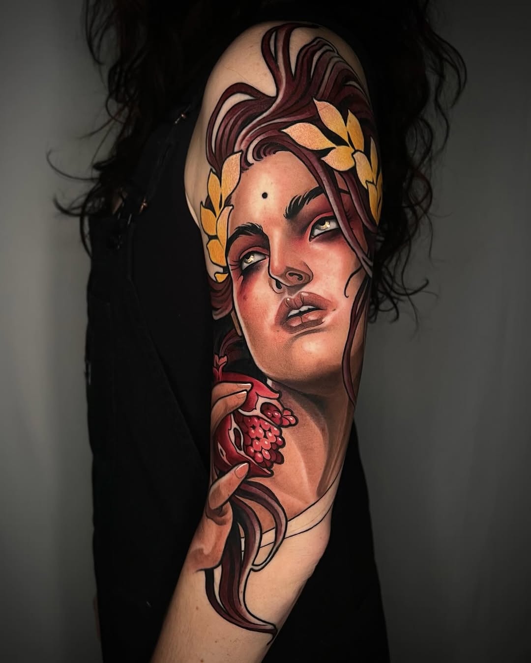 Portrait tattoo of a woman with burgundy hair and gold leaf crown on upper arm, featuring red berries and flowing linework.