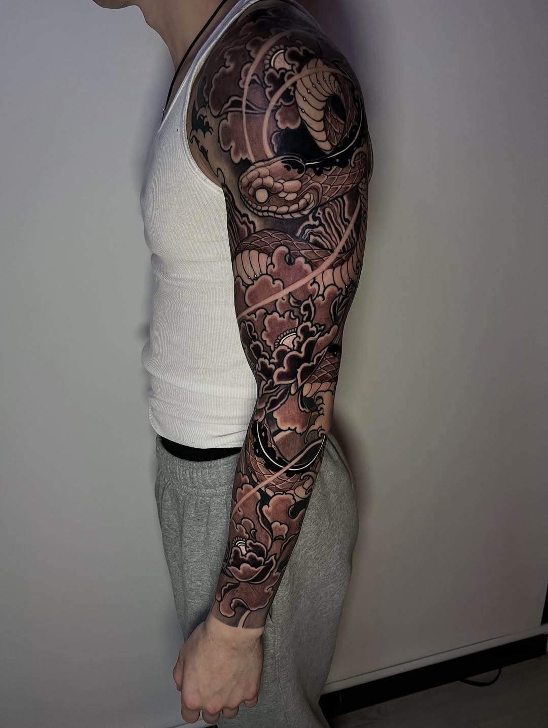 Full arm sleeve tattoo featuring ornate clouds, waves, and mythological figures in brown and black ink on a person's right arm.