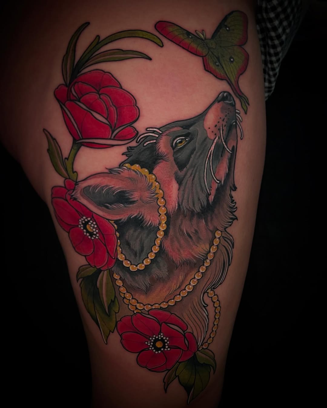 Possum wearing beaded necklaces surrounded by red flowers and a green moth, tattooed on the thigh in red, green, gold, and black.