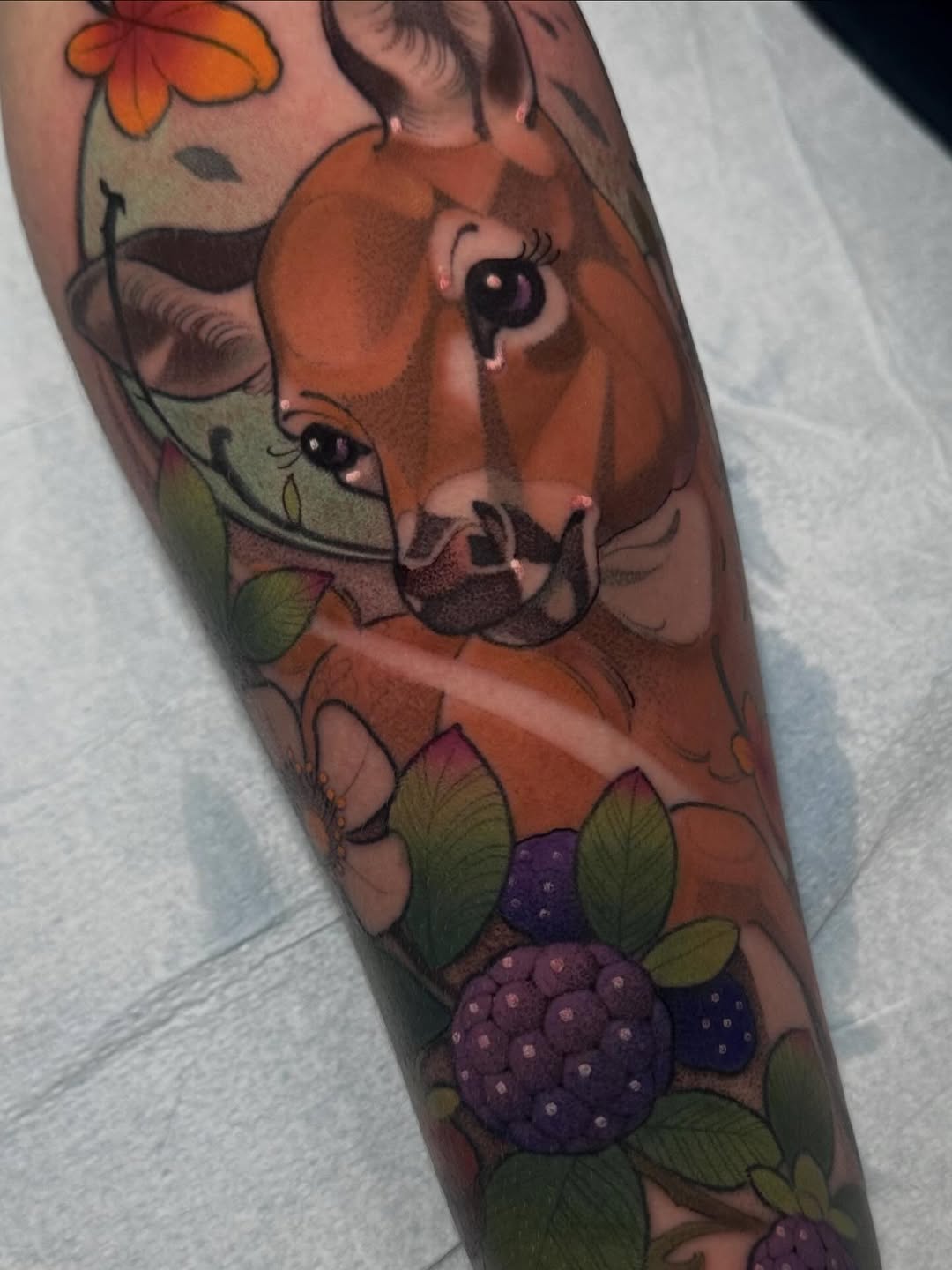 Colorful arm tattoo featuring a brown cow's face with expressive eyes and blackberries with green leaves below on the forearm.