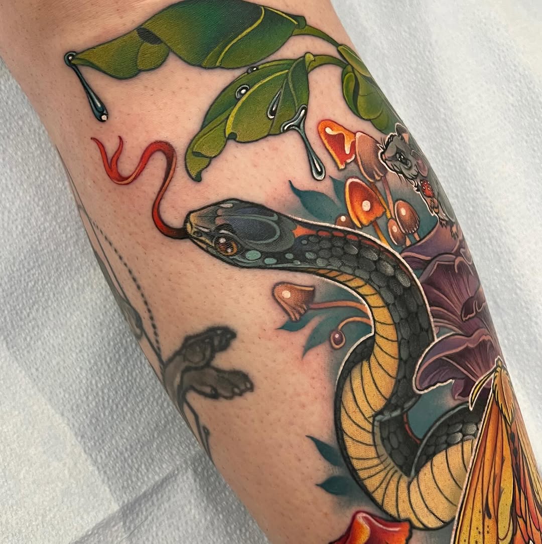 Colorful snake tattoo on calf featuring a black serpent with yellow belly scales, green leaves, red flowers, and orange blooms in vibrant hues.