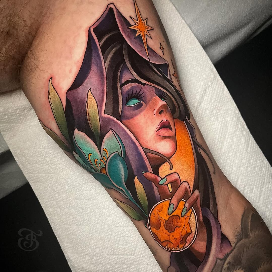 Colorful arm tattoo featuring a hooded figure with turquoise eyes holding an orange orb, surrounded by purple petals and a golden star.