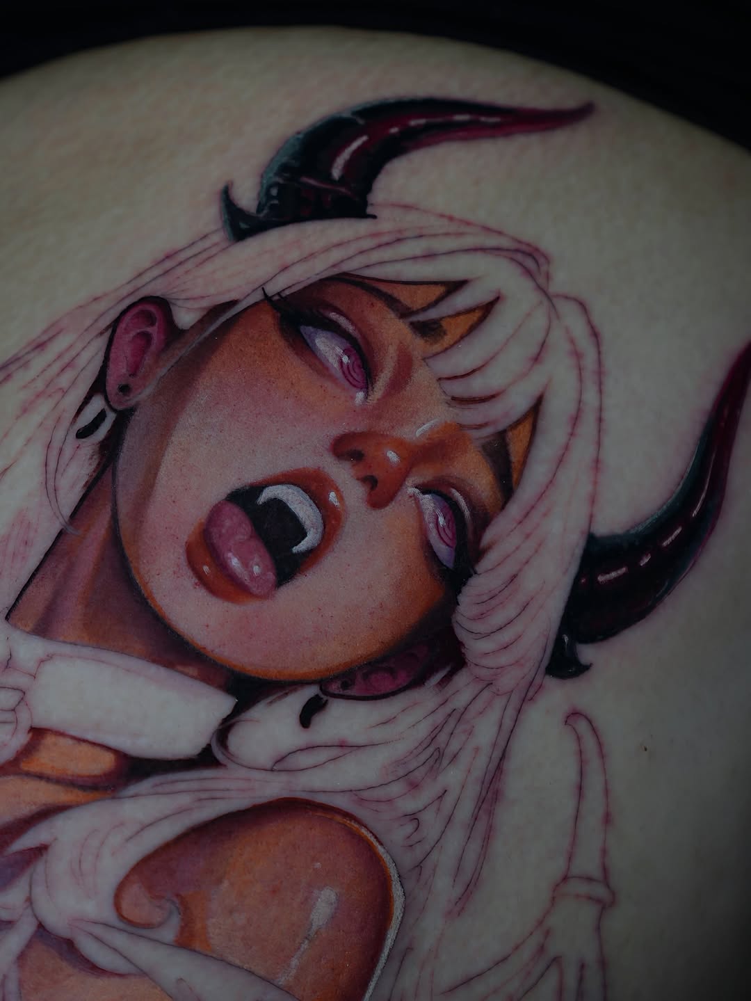 Colorful shoulder tattoo depicting a character with pink hair, horns, and exaggerated facial features in shades of pink, orange, and black.