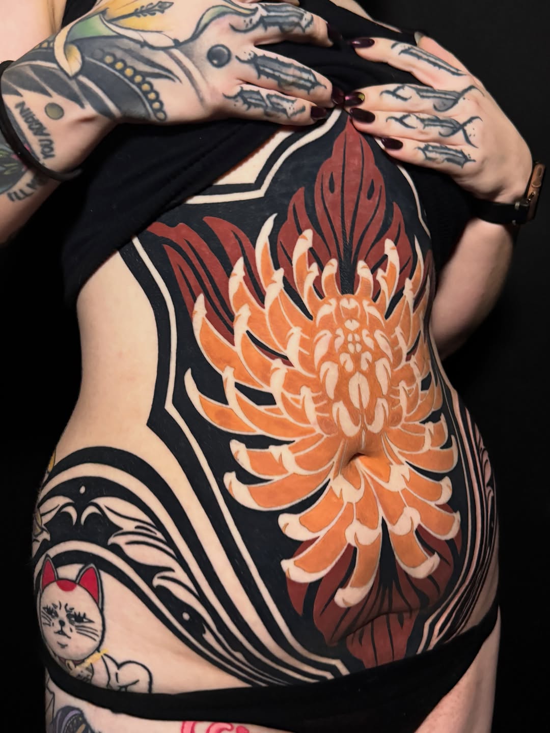 Large orange and red chrysanthemum with black outlines and decorative black linework covering the torso and ribcage area.