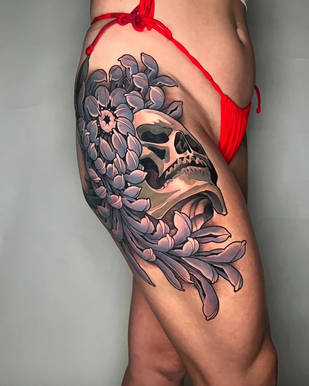 Skull with large peony flower on thigh, rendered in purple and grey tones with black outlines and shading details.