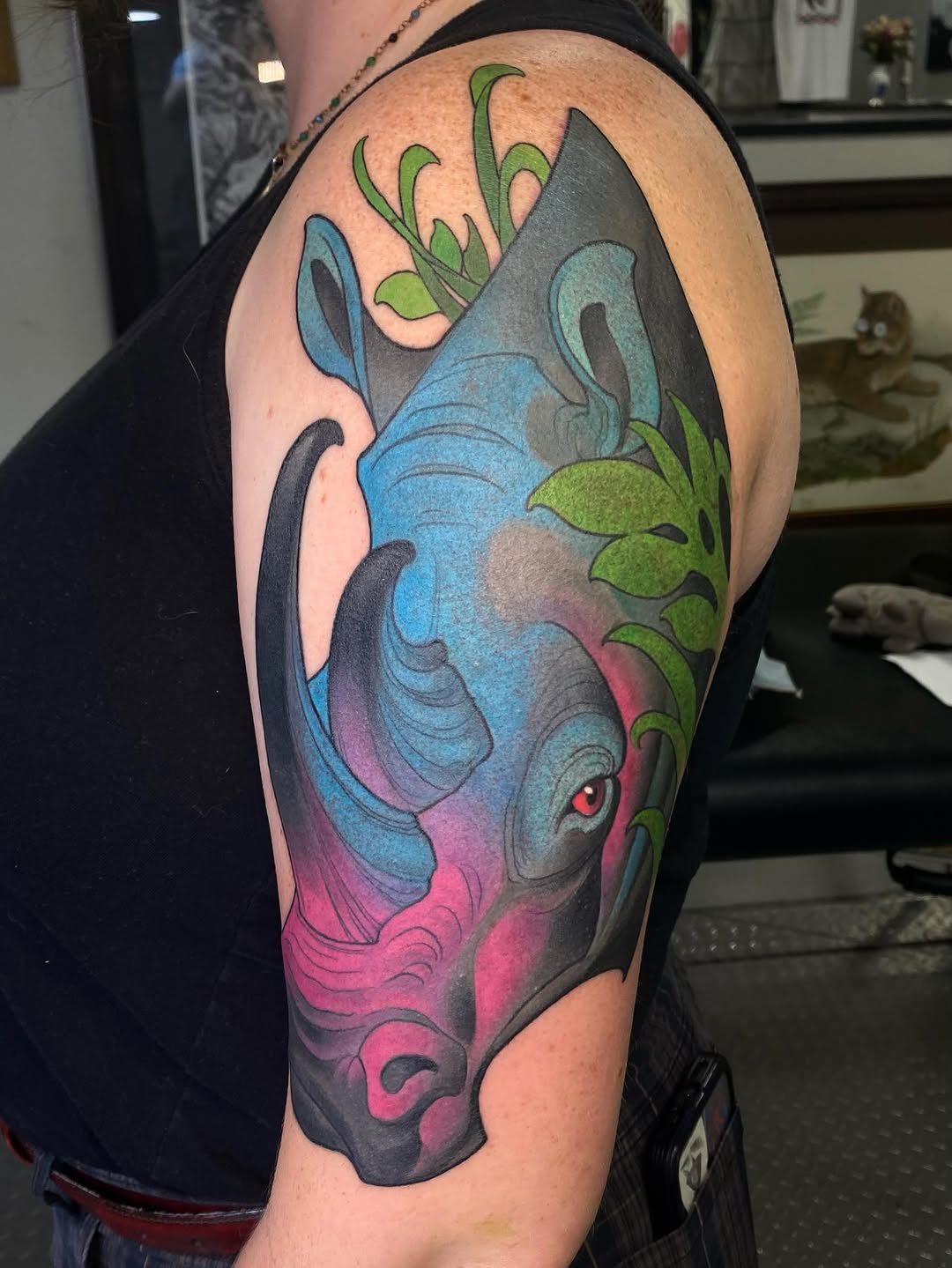 Colorful fish head tattoo on upper arm featuring blue, pink, and green tones with flowing fins and aquatic plant elements.